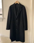 A charcoal wool overcoat hanging on a wooden hanger in an apartment