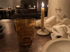 Amber glassware, rumpled cream linen, and a beeswax candle on a dark restaurant table